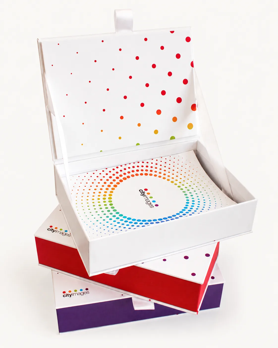 Stack of rigid presentation boxes in white, red and purple with rainbow dot artwork, top box open showing a printed interior