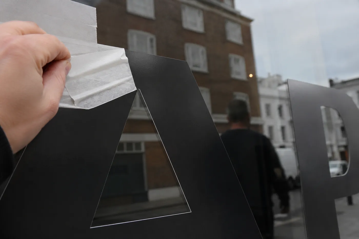 Fret cut vinyl letter with application tape being positioned on shop-front glass in London