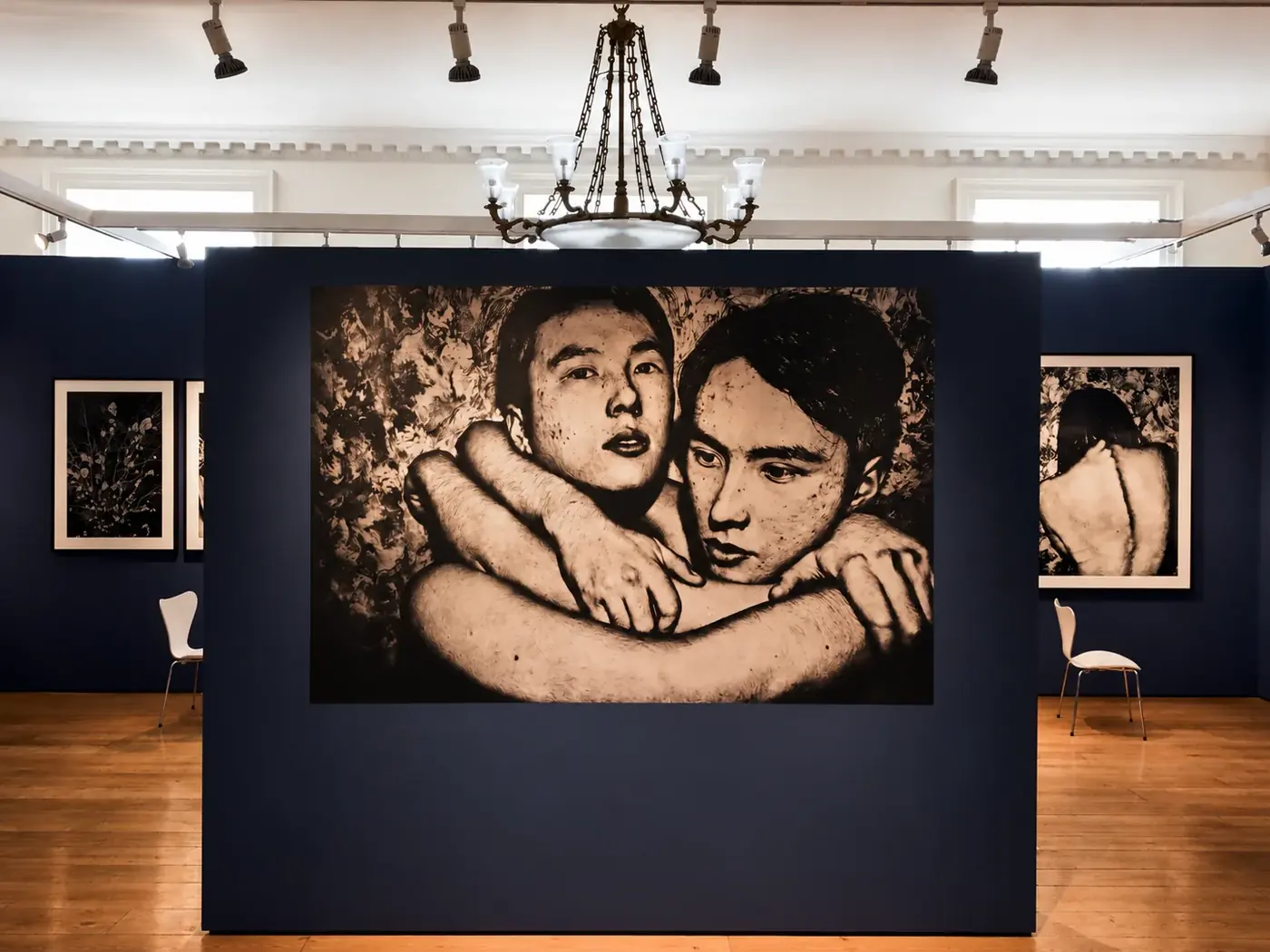 Large monochrome portrait printed and mounted on a navy gallery wall with framed works either side