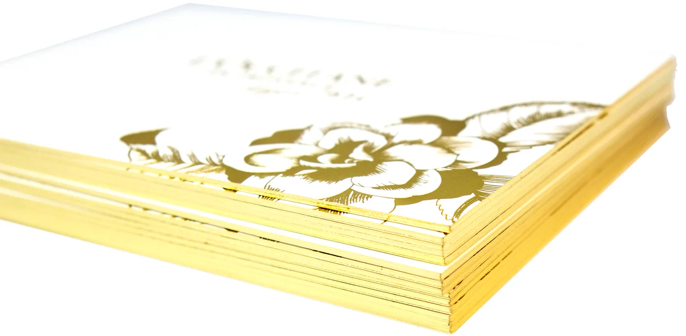 Stack of white invitations with gold foil artwork and gilded gold painted edges