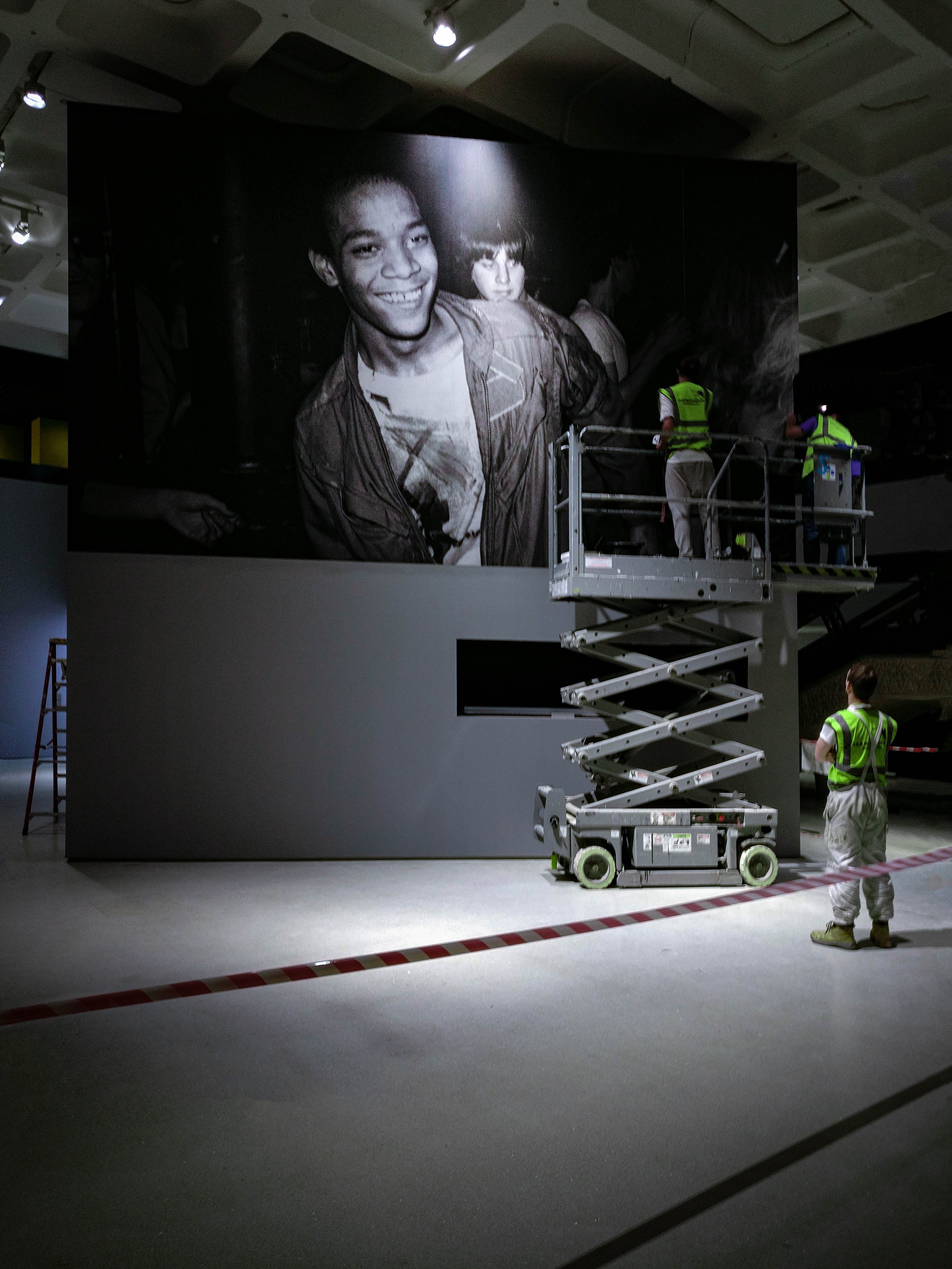 three men on a scissor ladder installing a large printed graphic for an event